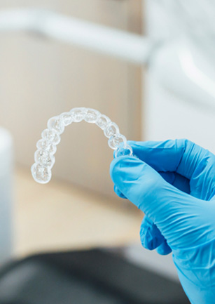 Dentist with blue glove holding clear aligner