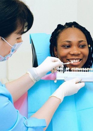 Dentist holding shade guide to woman’s teeth