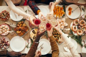 Hands clinking wine glasses together over a table of food