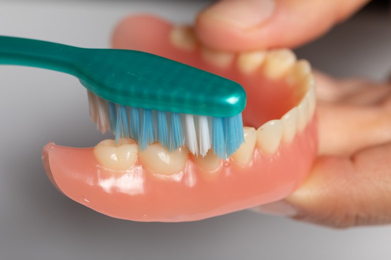 person cleaning dentures with toothbrush