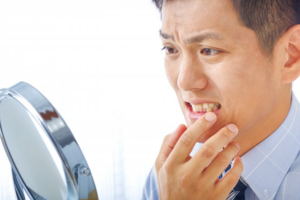 Man checking his teeth in a mirror and looking concerned