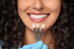 Gloved hand holding up 3 veneers to smiling woman.